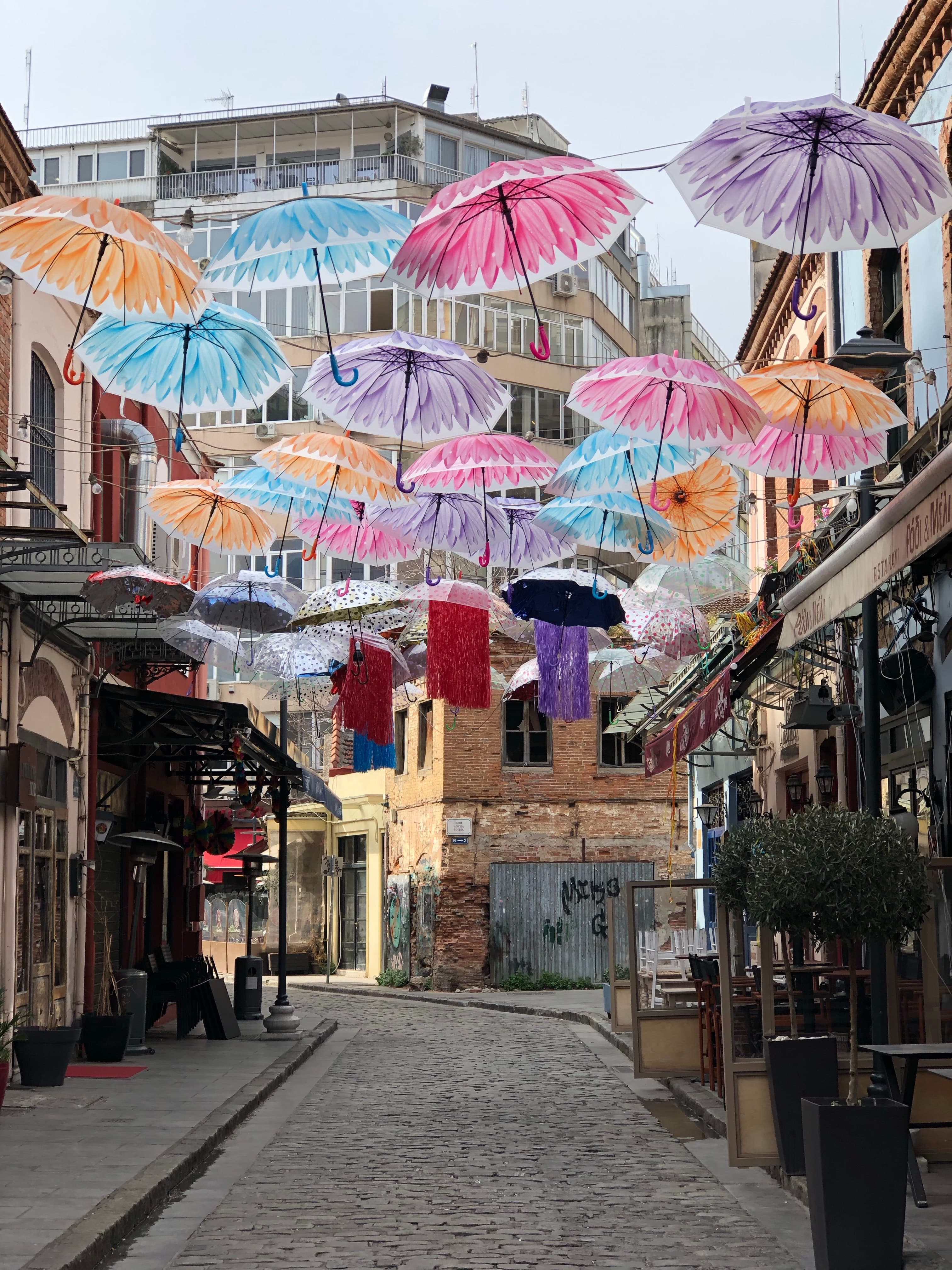Cobblestone alley with colourful umbrellas hanging overhead